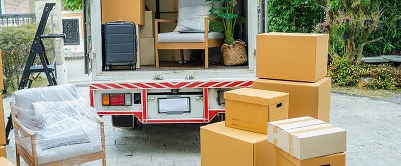 Camión de mudanzas abierto con muebles y cajas en la entrada de una vivienda