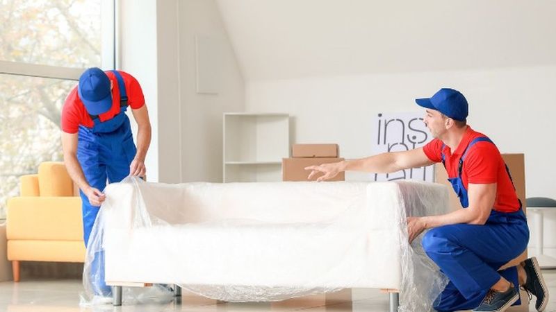Operarios de mudanzas cubriendo un sofá blanco con una funda protectora