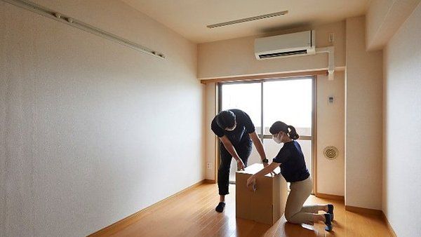 Dos personas cerrando una caja de mudanza en un piso vacío